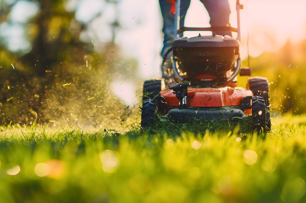Aufnahme aus niedriger Perspektive eines Mannes, der an einem sonnigen Sommer- oder Frühlingstag in seinem Garten im Freien mit einem Garten- oder Heckenschneidgerät Gras schneidet oder stutzt. Arbeiten zur Hauspflege oder Hobby, Freizeitbeschäftigung
