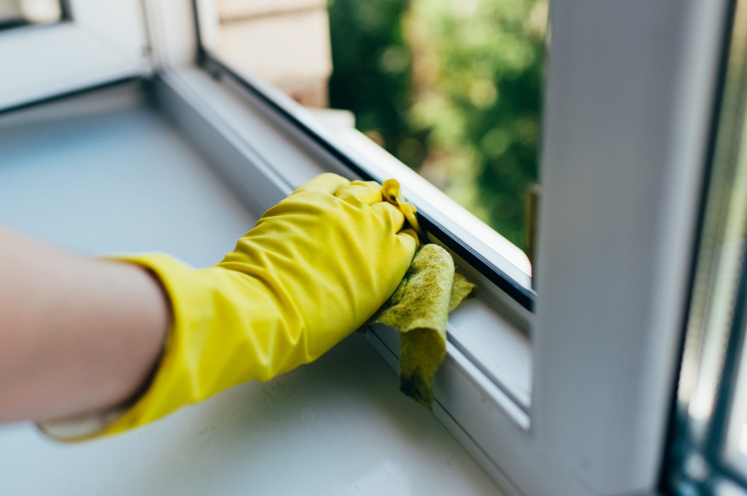 Eine Person mit Handschuhen wischt den Fensterrahmen mit einem Reinigungstuch ab